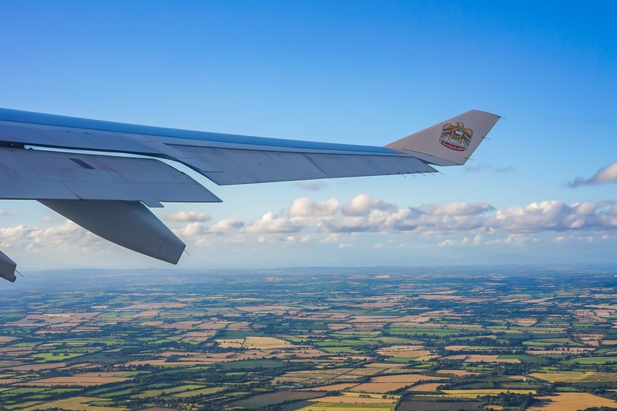 Image of an airplane flying over Ireland, Green fields in the background and only the airplane wing on view 